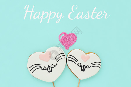 动物欢乐复活节贺卡两个姜饼干在一根棍子上的两杯姜饼以心脏的形状画着兔子脸和闪亮的心在蓝色背景上假期投标图片
