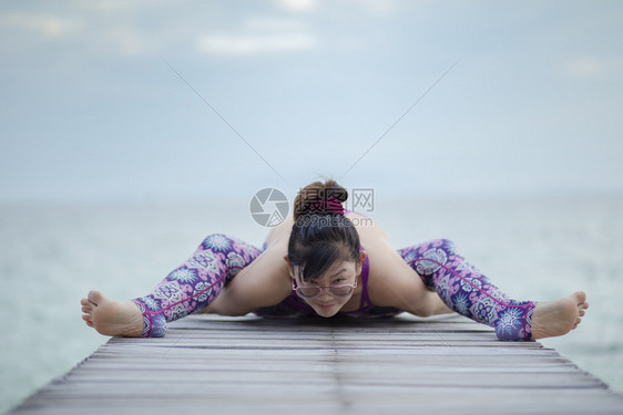 美丽的女人在海木码头做瑜伽在海龟上摆姿势假期海滩活动图片