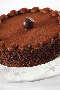 一张巧克力蛋糕上方有松露的美味巧克力蛋糕照片在一个盘子上贴着冰糖和雪花口音焦点在前边黑暗的富有白色图片