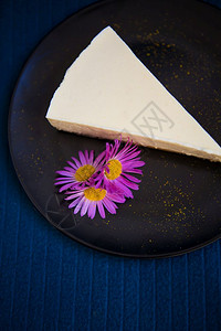 甜点食物披着紫花的奶油乳酪蛋糕涂在黑色盘子上的紫花朵涂在黑色盘子上的紫花朵乳制品图片