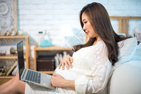 妈使用笔记本电脑坐在家中床上的怀孕亚洲妇沙发坐着图片