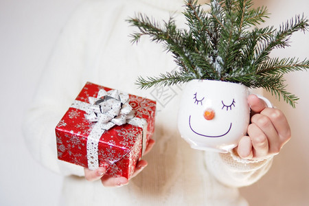 假期白雪皑一个穿着白毛衣的女孩拿着一个白色的杯子脸上有雪人角和红树枝还有色的礼物盒明信片图片