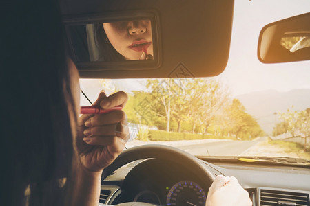 坐着女人在驾驶汽车时用口红做脸孔不安全行为多任务处理女孩图片
