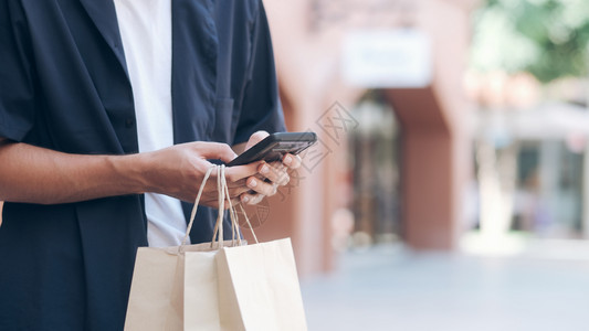 正在做有购物袋的青年男子在购物时使用手机购买移动电话尽管晋升图片