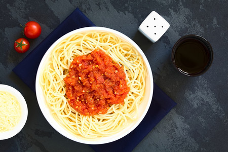 传统的意大利面粉和马里纳拉意大利面碗里加番茄酱红葡萄酒和边涂奶酪用天然光照着板的顶部磨碎营养拍照图片