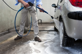 男子用高压水喷气式飞机在洗车的摊位上摇晃他汽车漂洗软管喷涂图片