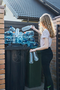户外进入空的将废旧塑料水瓶扔进垃圾桶的年轻妇女把空用塑料瓶丢弃在垃圾桶里收集塑料废物以回收以便回收塑料污染概念和太多塑料废物图片