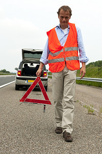 穿着安全背心从车后向行走的人携带警示三角形破碎的高速公路信号图片