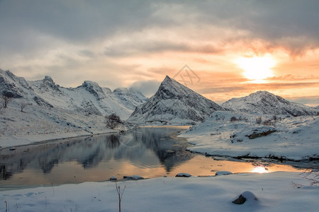 北极天空挪威峡湾的小海周围环绕着积雪的山峰冬季傍晚挪威渡湾在日落冬山之间经过图片