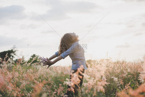 年轻美丽的女士站在草原上举起双臂在空中露出青草地日落时与大自然相享受女花潮人图片