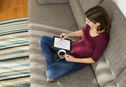 在沙发上家的漂亮女人用平板电脑工作在职的药片咖啡图片