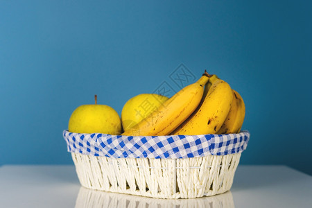 或者在蓝墙前桌边的白篮子里提取水果香蕉和苹白天有机食品素或者蓝墙背景维他命有机的图片