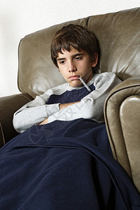 发烧生病的小孩坐在大皮椅上嘴里有温度计白种人睡衣图片