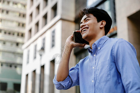 在城市中使用移动电话的年轻亚洲商人微笑城市中的移动电话数字城市阅读图片