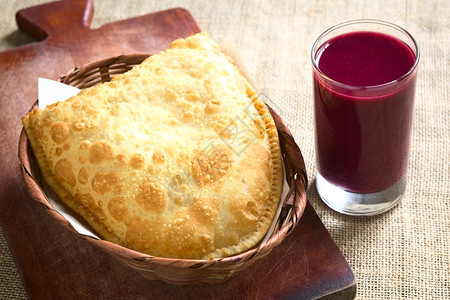 塞满美食玻利维亚传统小吃叫做派斯特尔深炸糕点和盛满奶酪的糕点配有木板上的紫玉米饮料Api木板上的紫玉米饮料用自然光拍攝图片