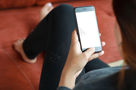 室内的近身女在沙发装饰上使用智能手机移动白色屏幕在线的空白图片
