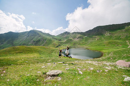 阶梯式年轻夫妇在大山谷中跳跃背景是冰川湖在乌埃斯卡的奥德萨自由概念爬坡道女士图片