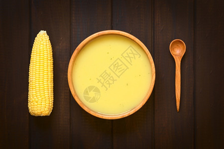 拍照黄色的木碗中玉米汤奶油夹头针面边有玉米椰子和木勺用天然光照在黑木上图片