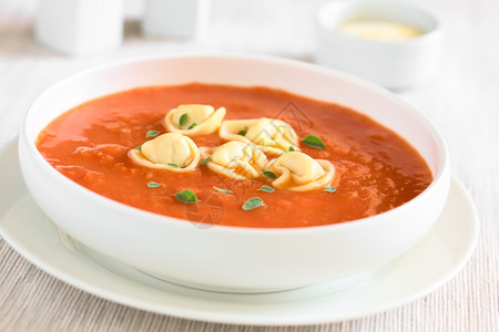 填充红色的土制番茄汤新鲜奶油用的红树叶充斥着托尔特利尼Tortellinni以天然光拍照选择焦点在汤中聚碗图片