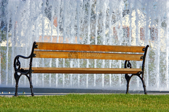 在喷泉前面公园的空木板凳上湿水色花园图片