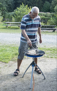花盆白种人景观男在露营时把食物和气体舒适的煤塞在一起图片