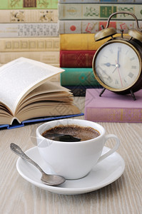 笔记本桌子上一杯咖啡背景是一本开着的书有时钟和一堆书图馆阿拉伯图片