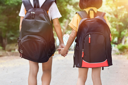 背着手的学生户外快乐的学习回到校两个姐妹生背着包手牵并一起上学的姐妹生教育概念背景