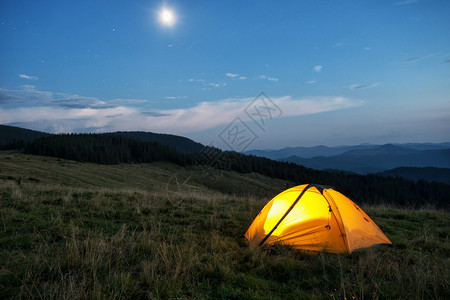 黄色的景观黑暗在黄昏山峰上红橙色帐篷从里面点燃天空月亮和星在黄昏的山峰上红橙色帐篷背景图片