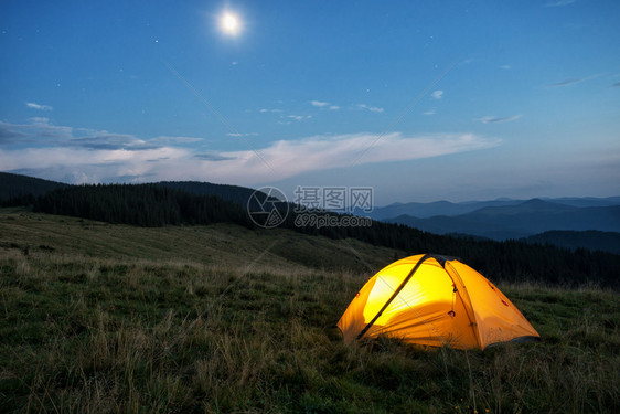 黄色的景观黑暗在黄昏山峰上红橙色帐篷从里面点燃天空月亮和星在黄昏的山峰上红橙色帐篷图片