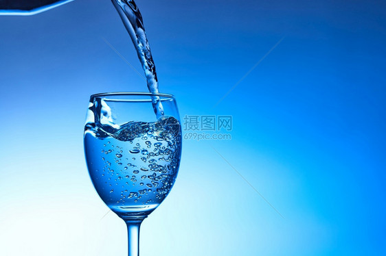 将水倒入玻璃中以蓝底为的玻璃杯喝寒冷瓶子图片