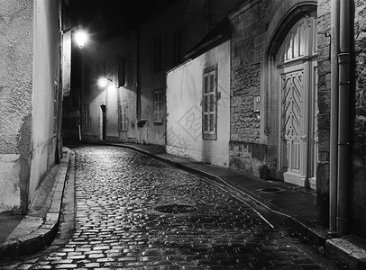 鹅卵石夜幕在法国波恩拍下一个空小巷那里湿的可白岩石闪耀着光芒与从街道灯光中轻视的亮相照从黑白胶片中扫描出来照明雨图片