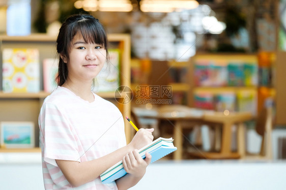 站在模糊图书馆背景前手拿书本的女学生图片