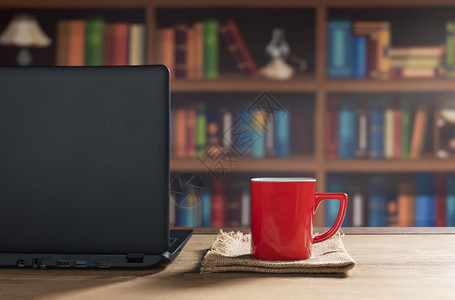 红咖啡杯在家庭办公室的木制桌上装有膝型电脑放松红色的复古图片