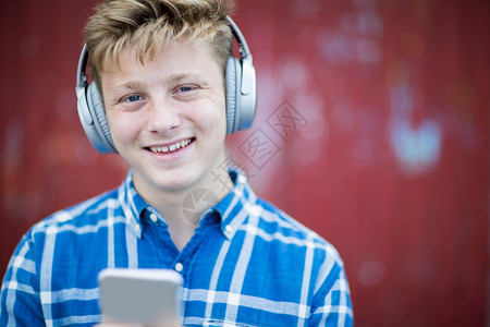 细胞城市环境中青少年男孩戴无线耳机和听音乐的肖像载于白种人消息传递图片