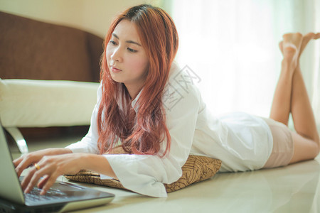 肖像在家里用笔记本电脑躺着的快乐亚洲年轻女子孩亚洲人图片