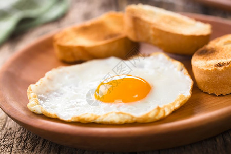 一个新鲜的煎蛋阳光明亮一面旁边有烤包饼切片放在木板上选择焦点聚在蛋前用烤面包炸鸡蛋黄早午餐自制图片