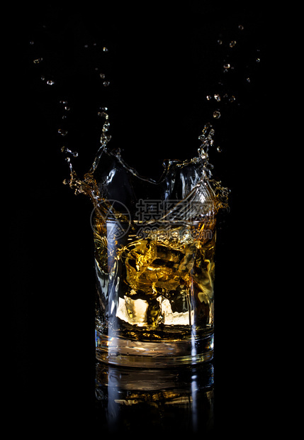 从一杯威士忌中的冰块上喷出隔绝在黑色背景的波浪上从一杯威士忌中的冰块上喷出浇注玻璃液体图片