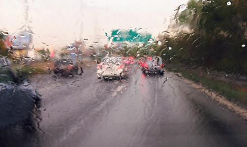 运输在大雨中驾驶一辆汽车在交通繁忙的风暴中驾驶一辆汽车路过风挡玻璃在开着车时有雨滴浅的城市图片