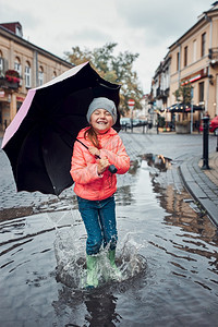 快乐的笑女孩拿着大伞跳在水坑里市中心散步雨阴凉的秋天小姑娘拿着大伞跳在水坑里雨中阴凉的秋天请享用玩正方形图片