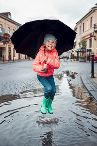 户外镇请享用快乐的笑女孩拿着大伞跳在水坑里市中心散步雨阴凉的秋天小姑娘拿着大伞跳在水坑里雨中阴凉的秋天图片