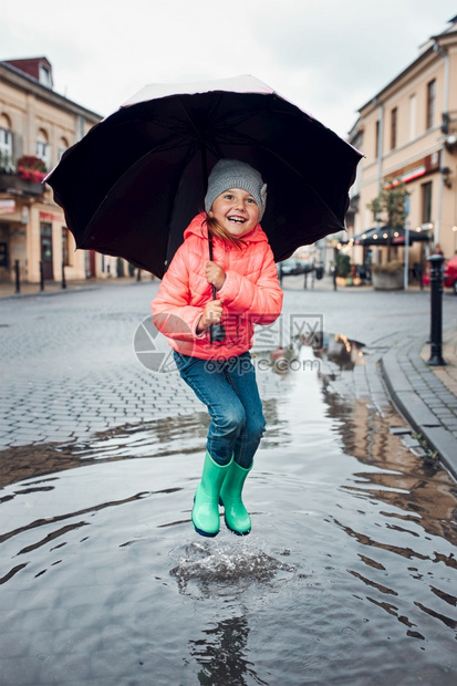户外镇请享用快乐的笑女孩拿着大伞跳在水坑里市中心散步雨阴凉的秋天小姑娘拿着大伞跳在水坑里雨中阴凉的秋天图片