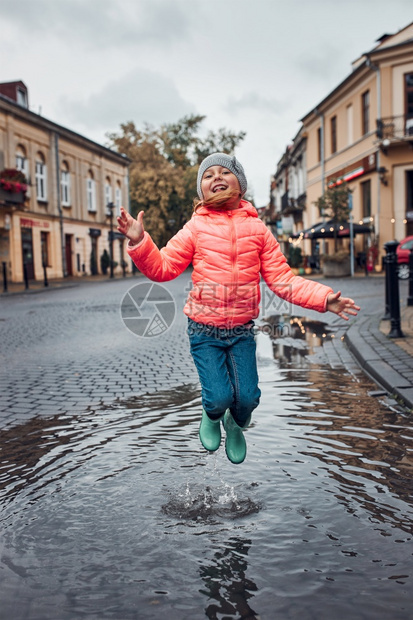 快乐的笑女孩在市中心散步时跳到水坑里在雨中阴凉秋天小姑娘在雨中阴凉秋天户外玩气图片