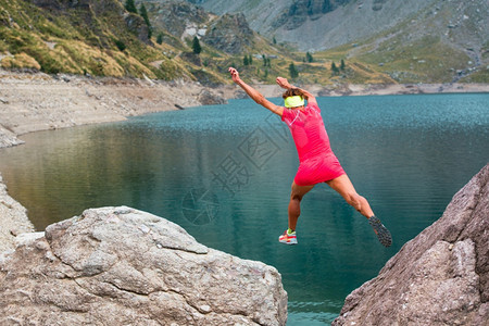 女士孩运动员在高山湖附近一个美丽的自然山上两块岩石之间跳跃腿成就图片