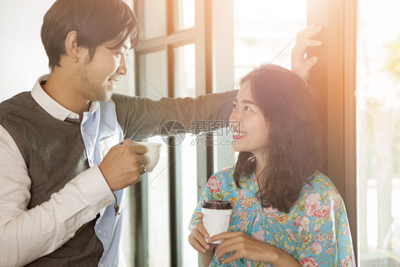 带着咖啡杯的年轻亚洲男女夫妇手握着含牙的咖啡杯微笑着脸面的快乐和轻松谈话幸福杯子郊游图片