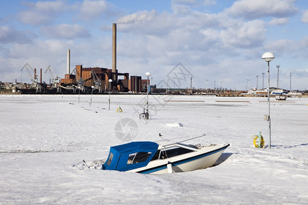 海滨一艘船在冬季中被困赫尔辛基冷冻港的停泊船只在这种背景下一个工业厂正在运营面雪图片