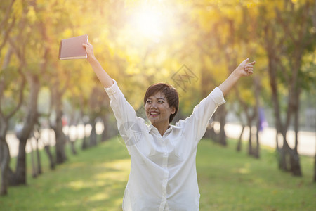 绽放夏天肖像年青女子和学生书的柔弱面容在夏季公园站着图片