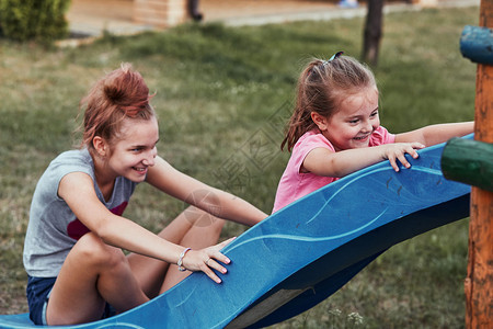 粘合兄弟年轻女孩在后院家庭操场上与妹玩耍的年青女孩快乐笑的姐妹们在夏日一起滑雪时玩得开心真实的人情况户外图片