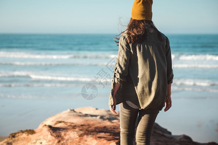 女人带着黄色的帽子走在悬崖上看海滩超过洋凉爽的图片