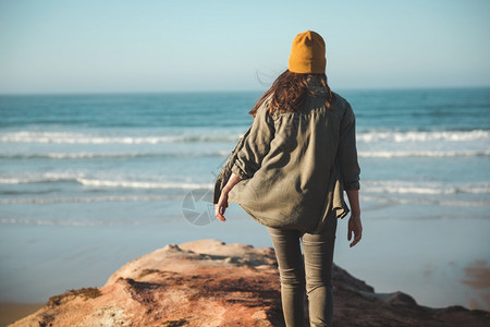 黄色女孩女人带着黄色的帽子走在悬崖上看海滩步行活动人们背景