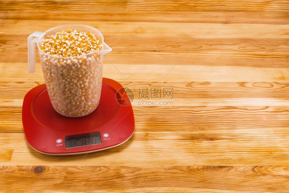 比率厨师电子的在天然木本底红色塑料电子规模的透明计量杯中玉米在一个具有复制空间的木材背景电子计量杯中将玉米放在一个带有复制空间的图片